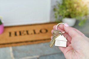 Holding the keys to a new house on the front porch with a HELLO welcome mat.