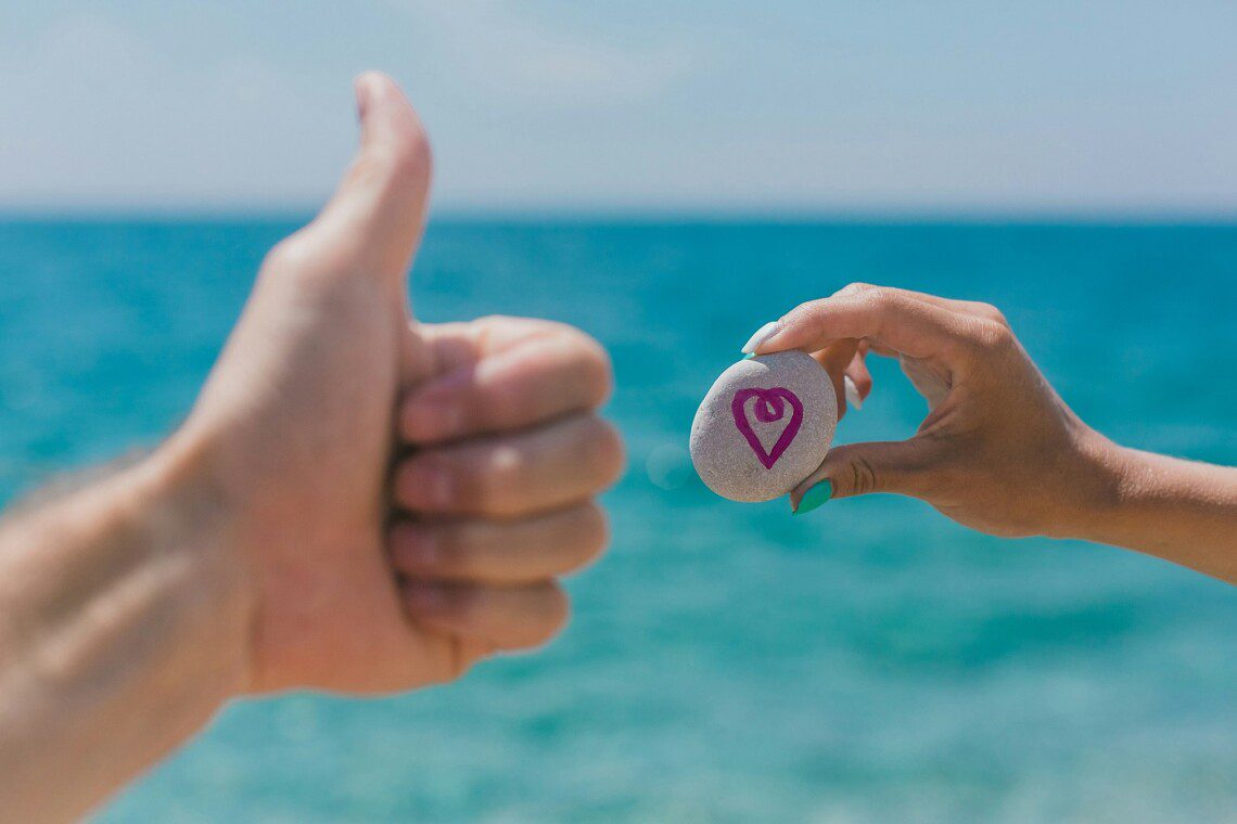 Pink hearth painted on stone with sea background. Love travel concept. Hand male and female